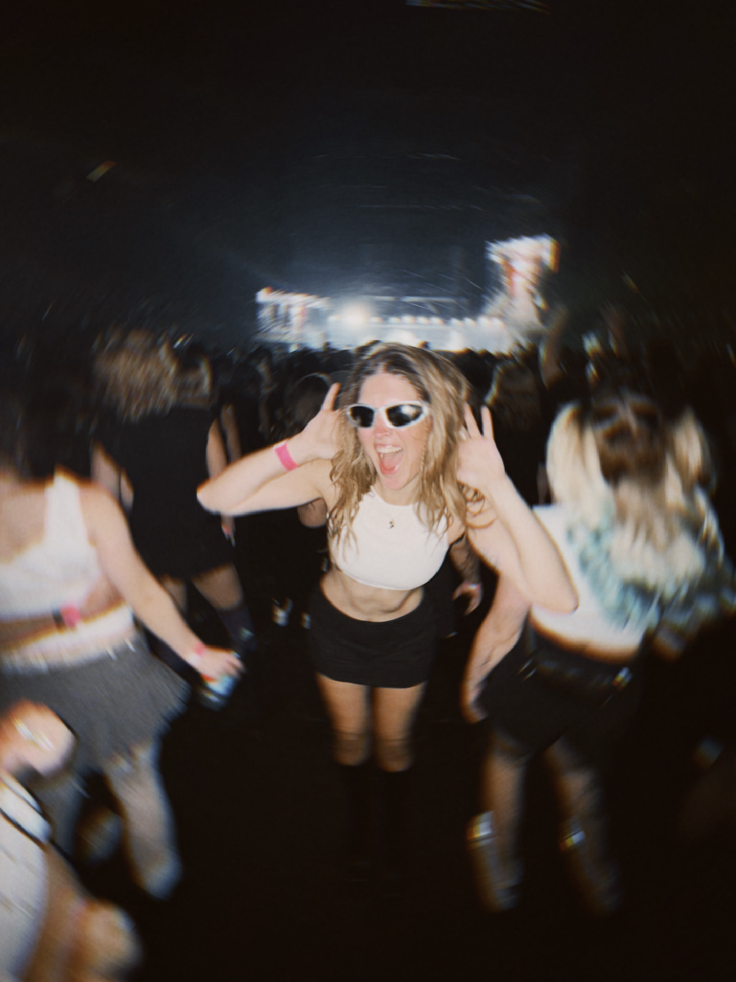 A friend laughing in white sunglasses in a dark crowd, direct flash film photo
