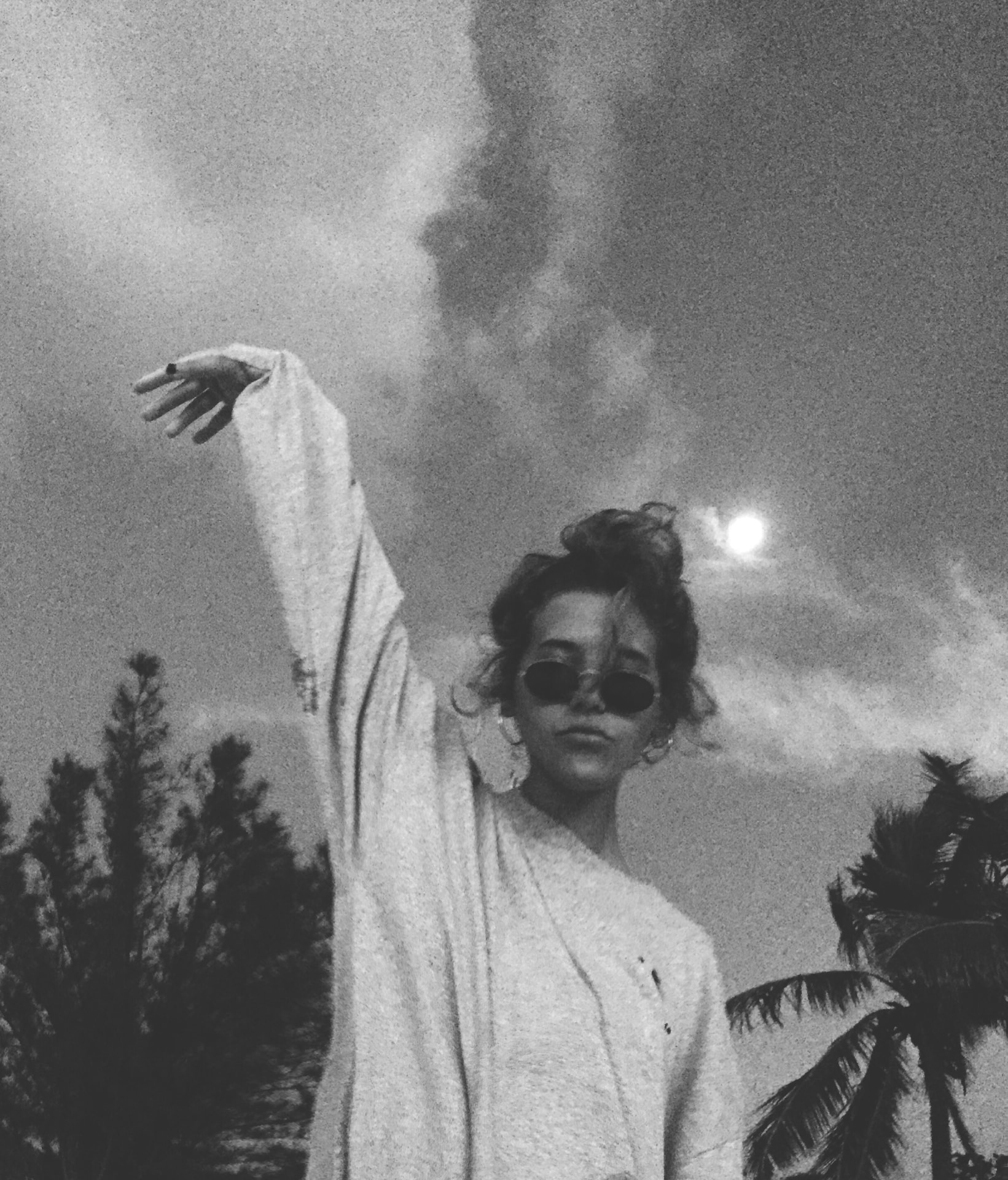 Woman posing beneath a cloudy sky and palm trees